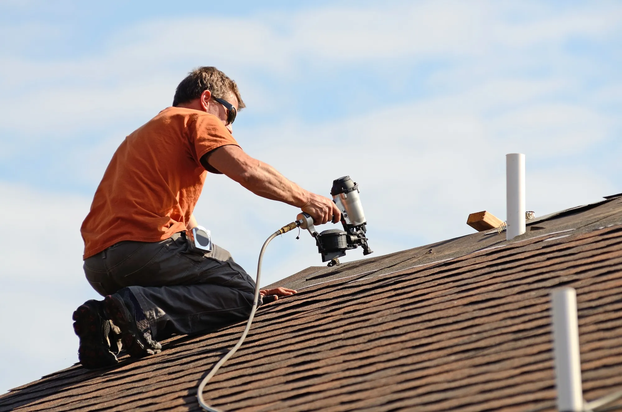 A roofer fastening shingles on a rooftop under a blue sky